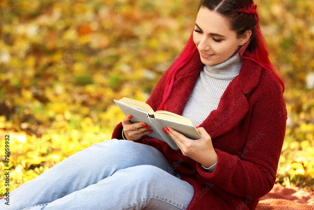 穿着保暖外套的美女在秋季公园看书