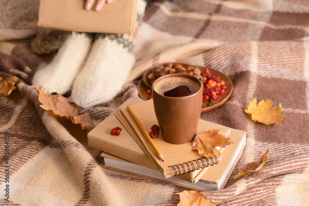 一杯褐色咖啡，背景是方格布，上面有书和秋叶