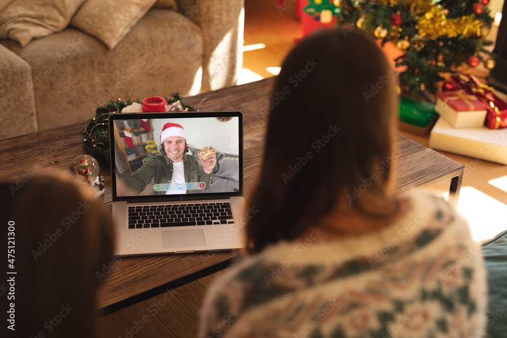 母女俩与戴圣诞老人帽的快乐高加索男子进行笔记本电脑圣诞视频通话