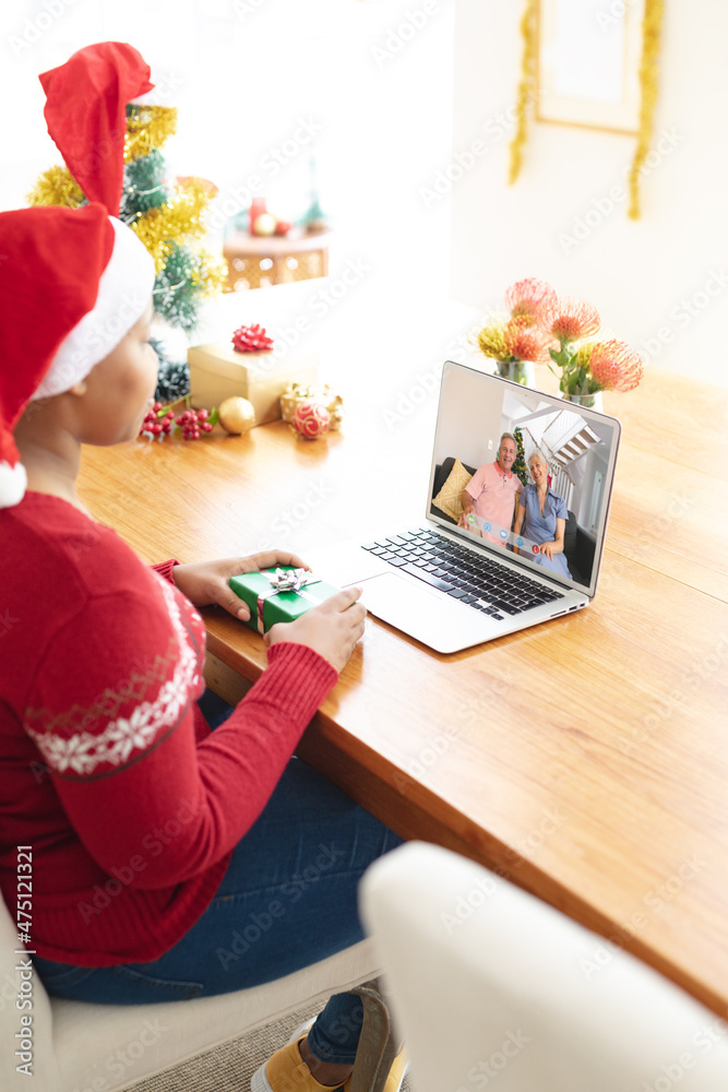 戴着圣诞帽的非裔美国妇女与高加索高级夫妇进行笔记本电脑圣诞视频通话