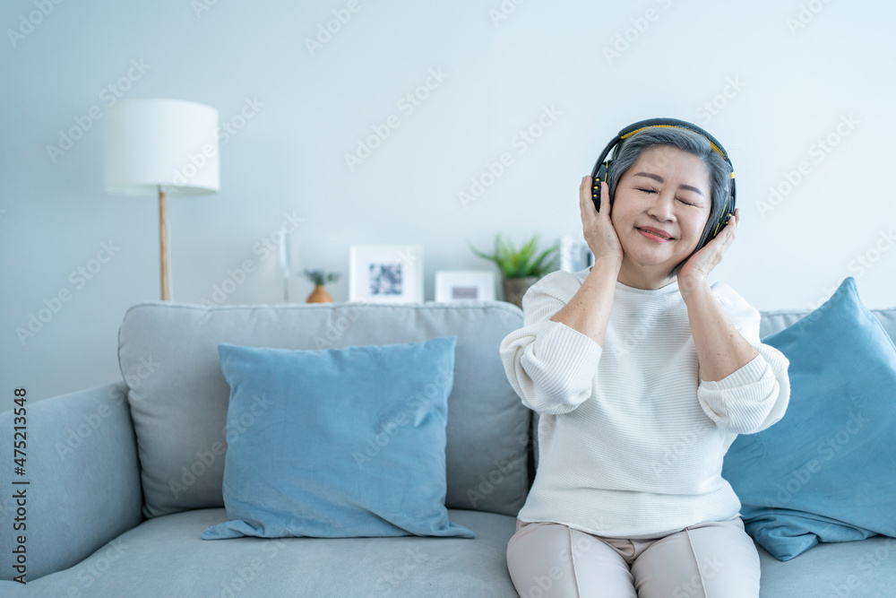 Asian senior mature woman enjoy listening to music and dancing on sofa