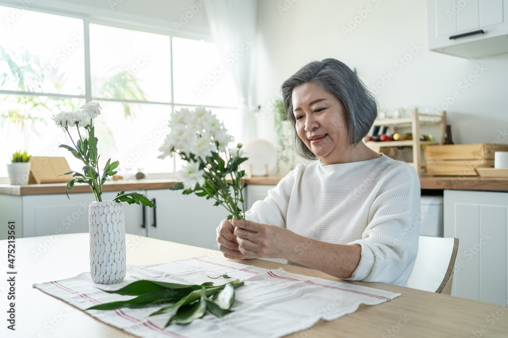 亚洲老年妇女在厨房里幸福地把鲜花放在花瓶上。