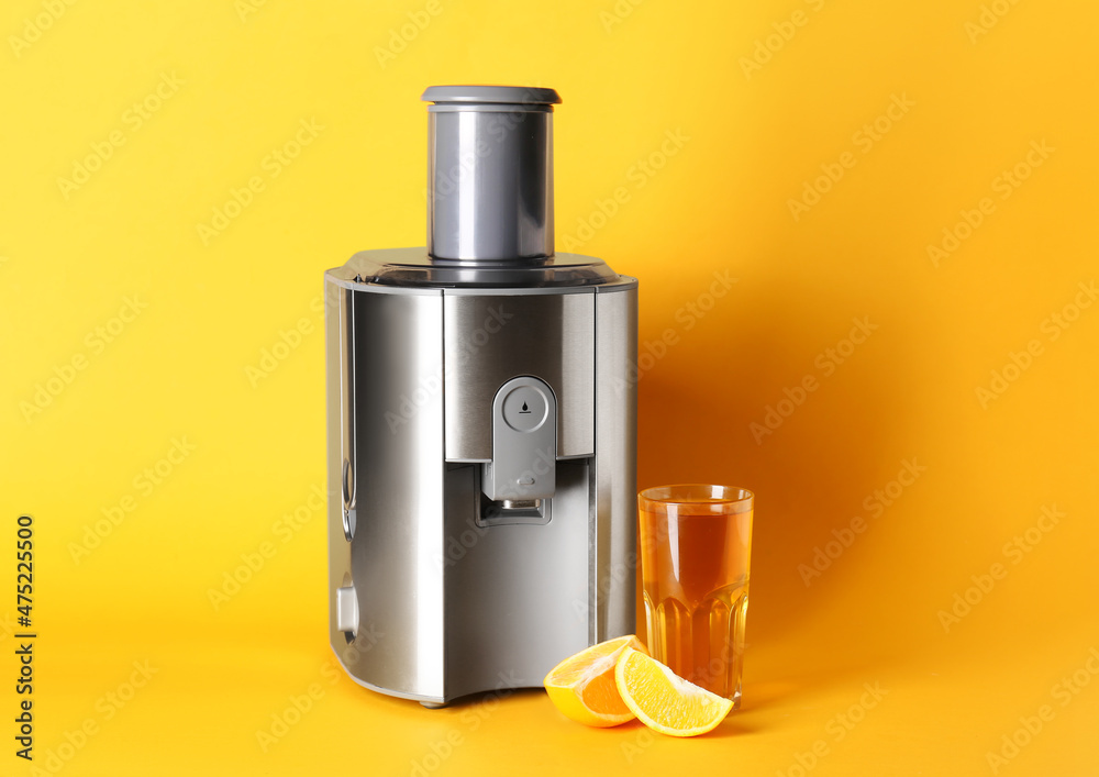 现代榨汁机，彩色背景上有一杯新鲜橙汁