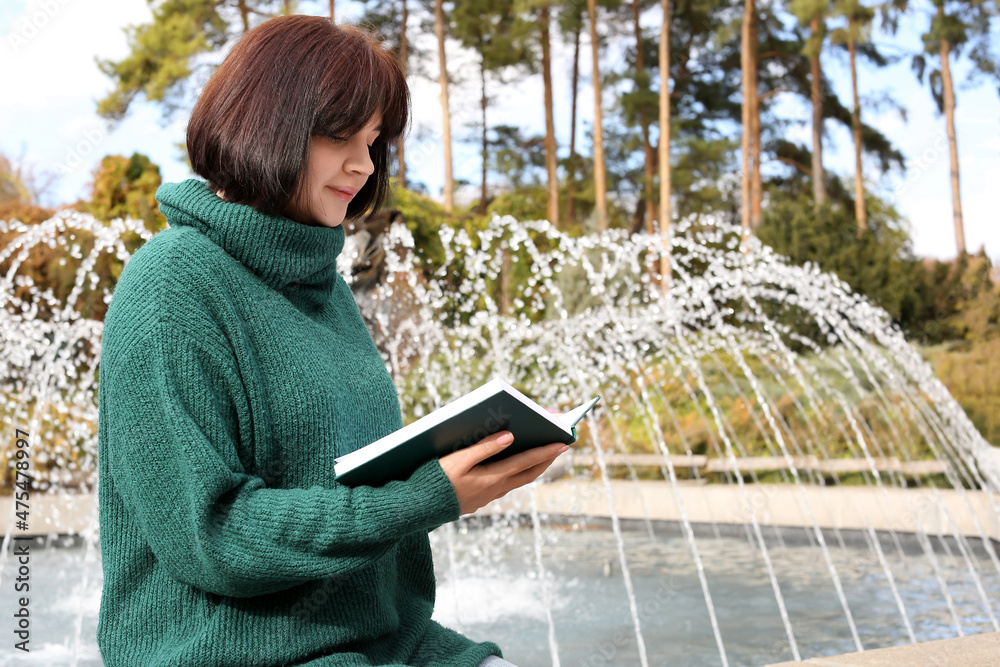 年轻美女在秋季公园喷泉旁看书
