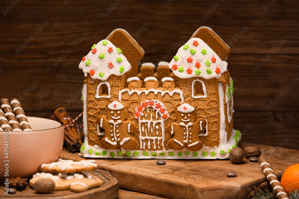 Board with beautiful gingerbread house on wooden background