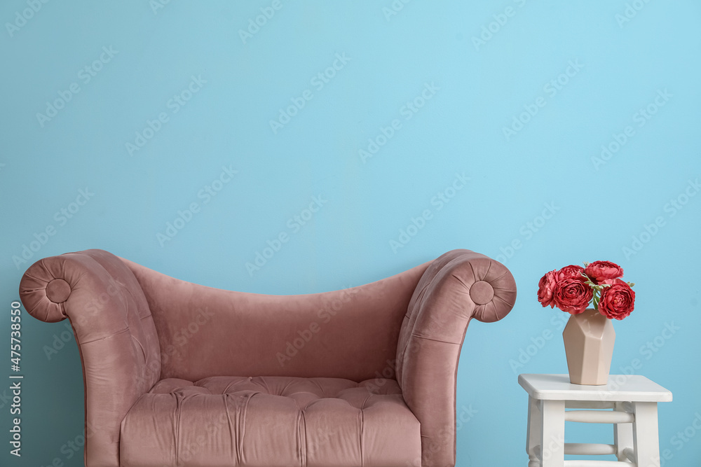 粉色扶手椅和花瓶，蓝色墙壁附近的凳子上有花