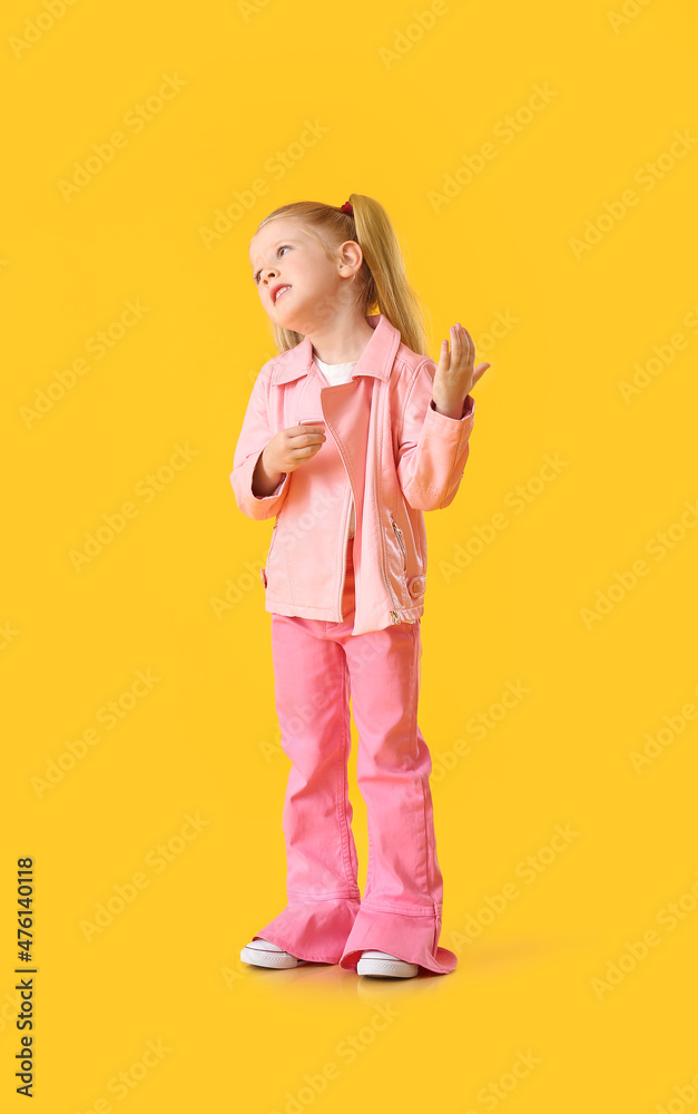 Cute little girl in pink jacket dancing on yellow background