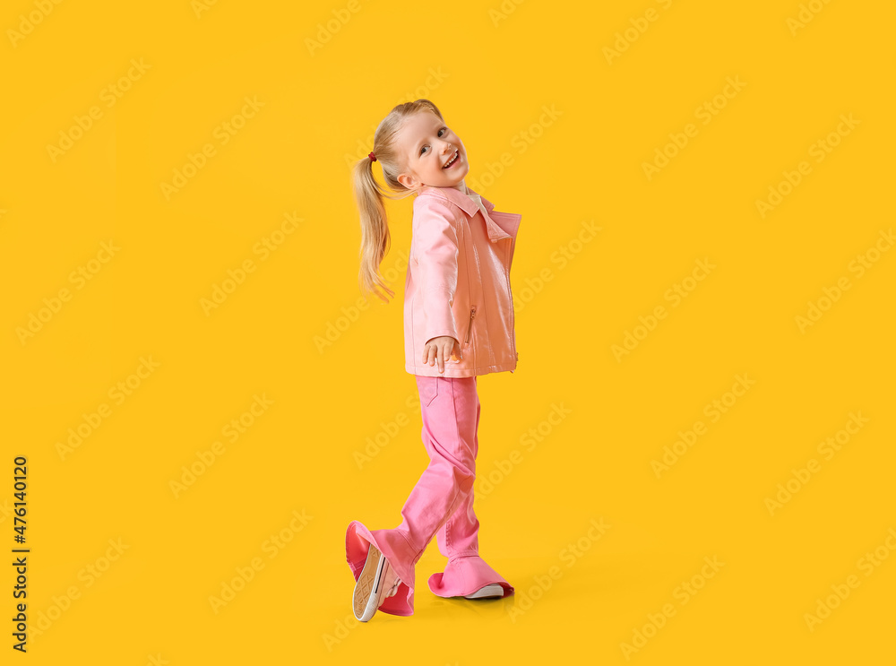 穿着粉色夹克在黄色背景下跳舞的可爱小女孩