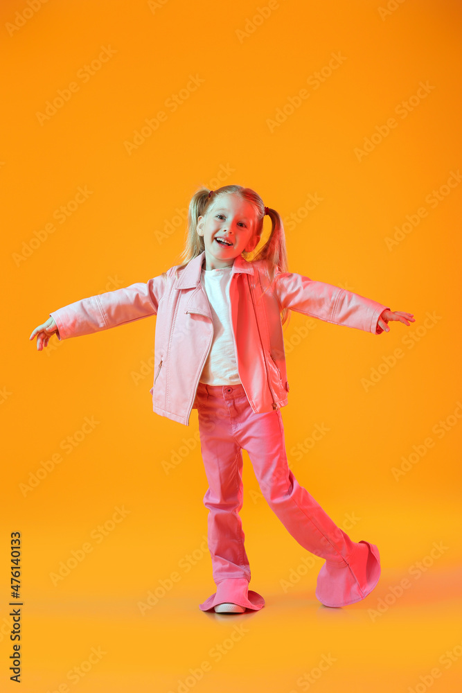 穿着粉色夹克在橙色背景下跳舞的可爱小女孩