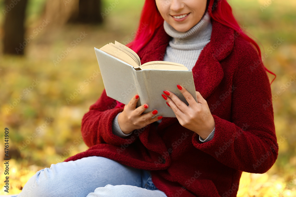 Beautiful woman with warm coat reading book in autumn park