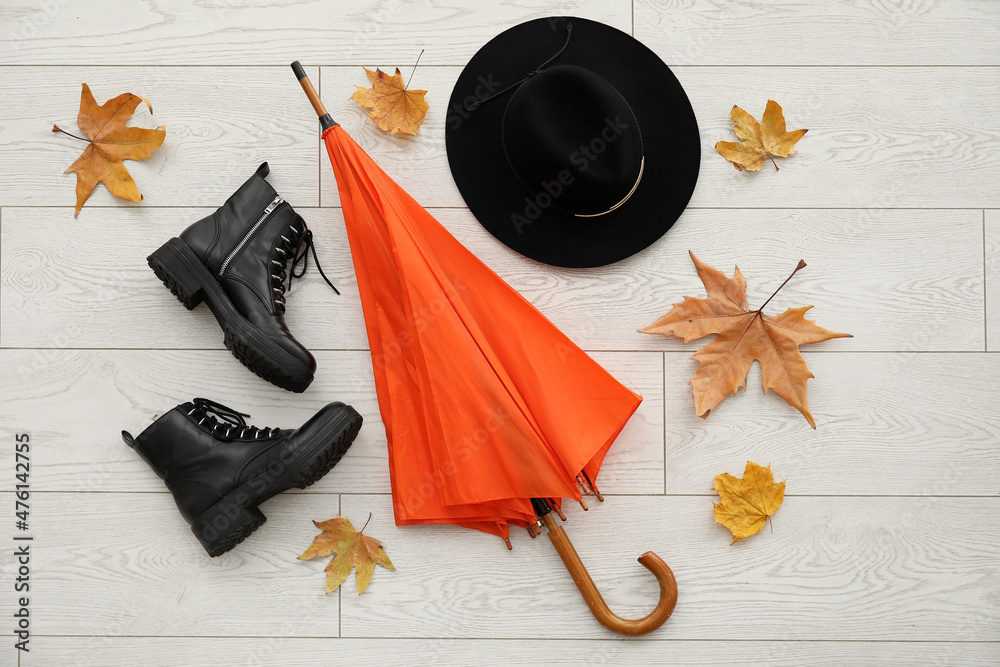浅色木质背景上的雨伞、鞋子、帽子和秋叶