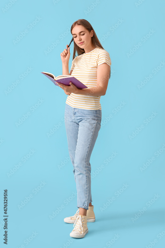 漂亮的年轻女人，拿着钢笔和蓝色背景的笔记本
