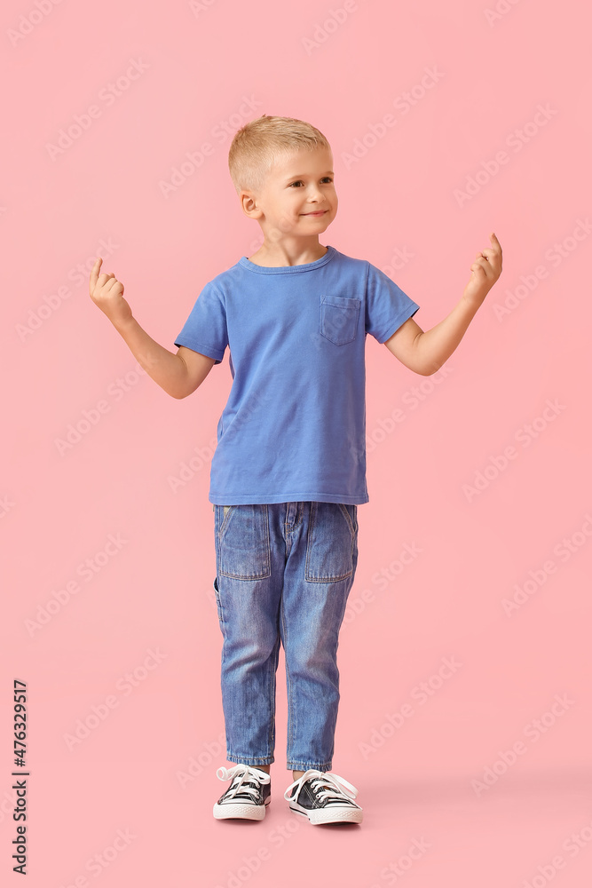 穿着蓝色t恤的可爱小男孩指着粉色背景上的东西