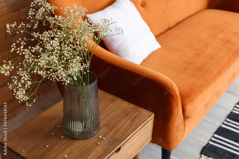 Vase with gypsophila flowers on wooden table and sofa near brick wall
