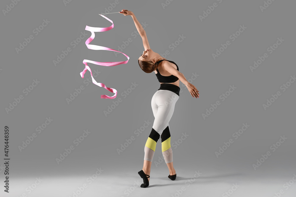 Beautiful young woman doing gymnastics with ribbon on grey background