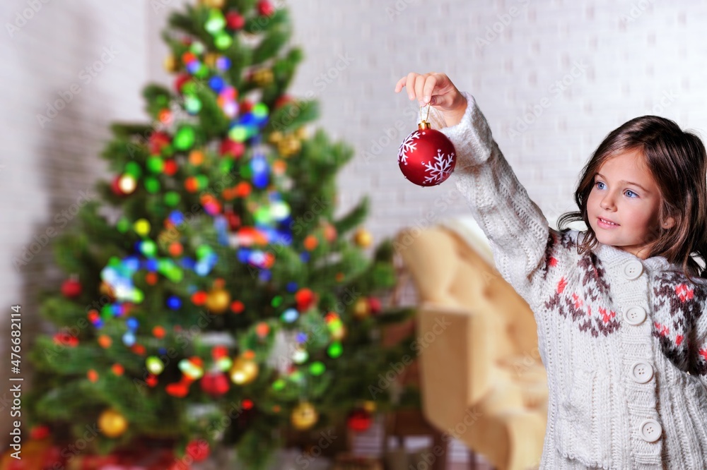 一个女孩的肖像在家里用玻璃球装饰圣诞树。
