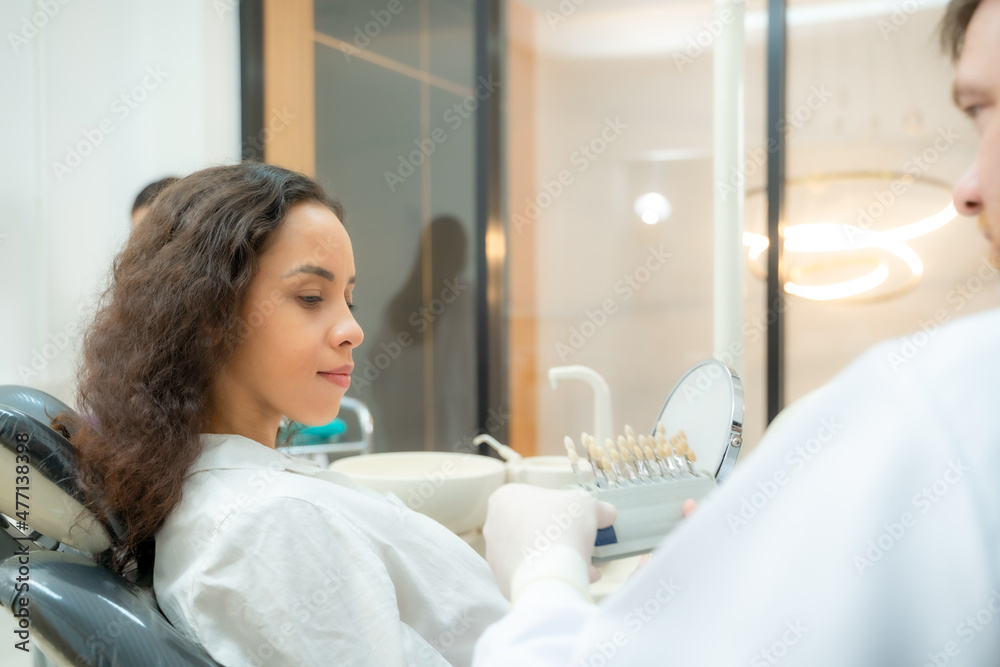 牙医使用牙科设备检查女性患者的牙齿，将牙齿与样本进行比较