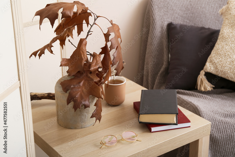 房间木桌上的秋枝、书籍、眼镜和一杯茶