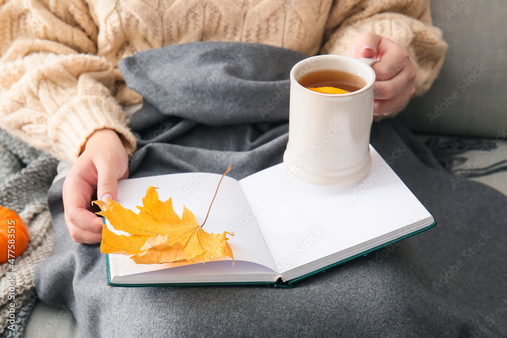 Woman holding cup of tea, opened book and autumn leaf, closeup