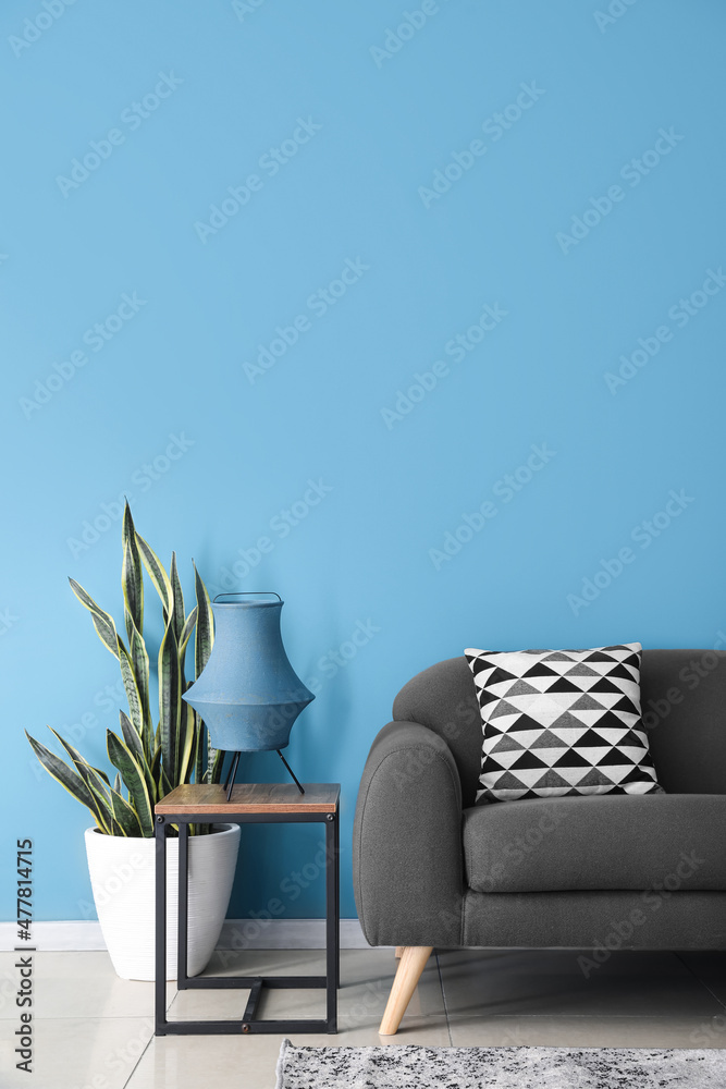 蓝色墙壁附近的桌子、室内植物和沙发上的时尚灯具
