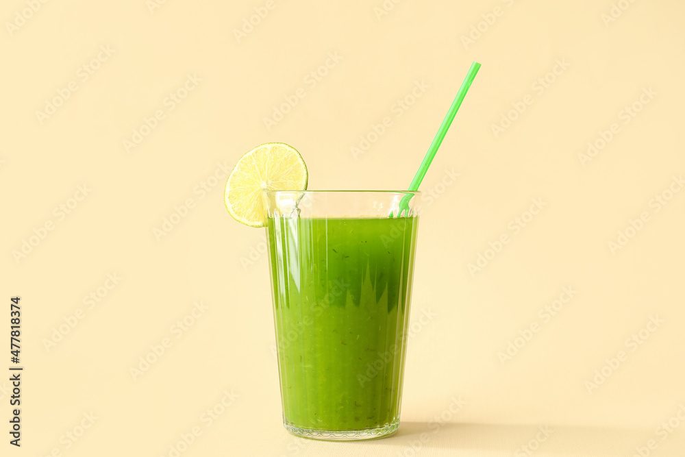 Glass of green juice with straw and lime slice on beige background