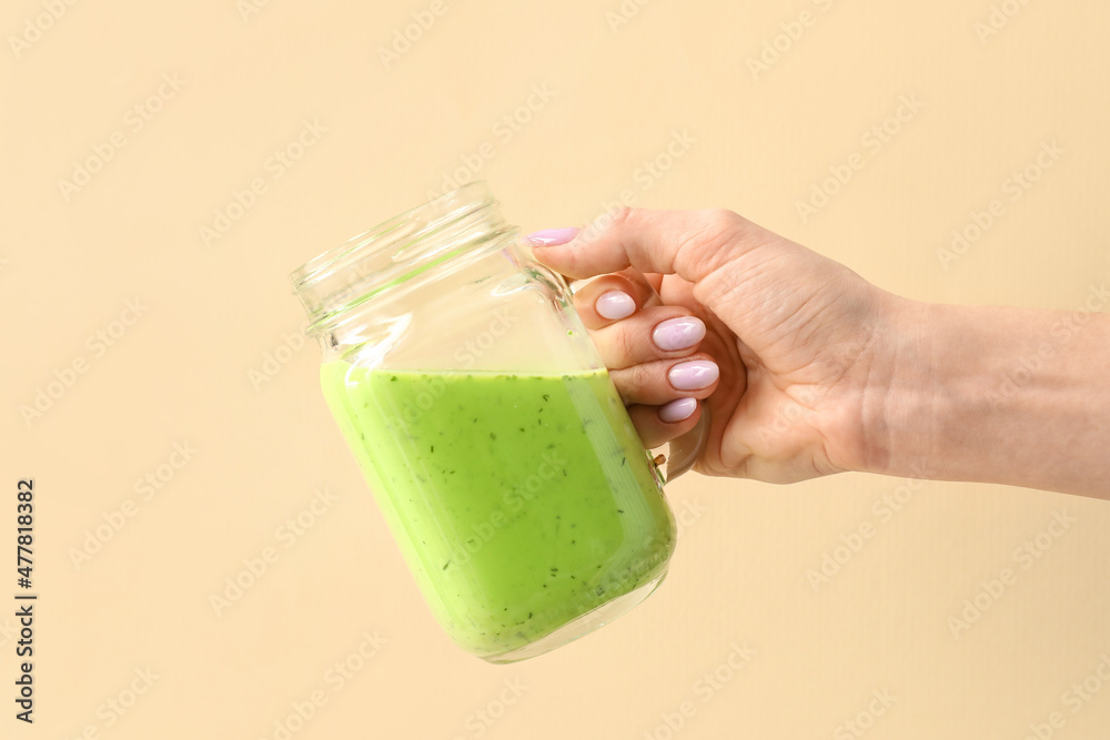 女人拿着一罐米色背景的绿色果汁