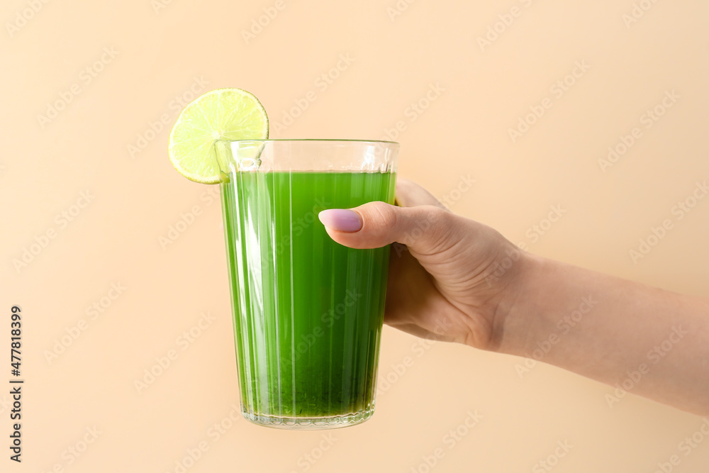 女人拿着一杯绿汁，米色背景上有莱姆片