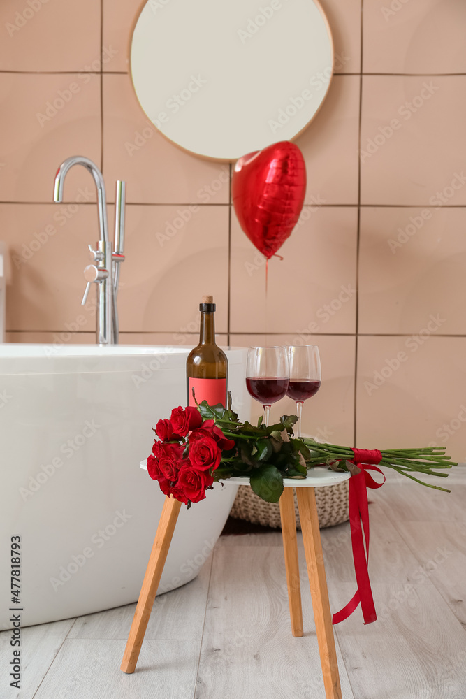 为情人节装饰的浴室桌子上放着装有葡萄酒、瓶子和花束的玻璃杯