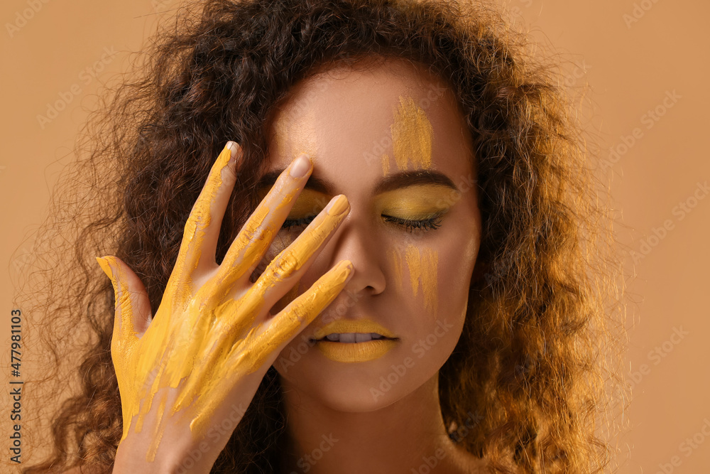 美丽的年轻女子，脸上和身上都涂着黄色的颜料，背景是彩色的