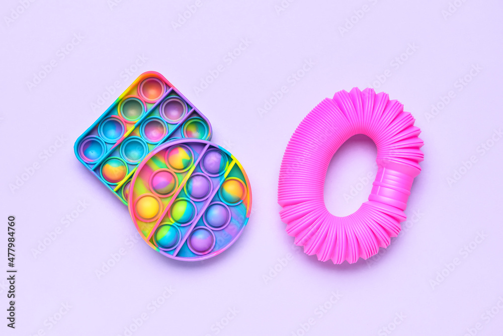 紫色背景下的彩色Pop Tube和Pop-it坐立不安的玩具