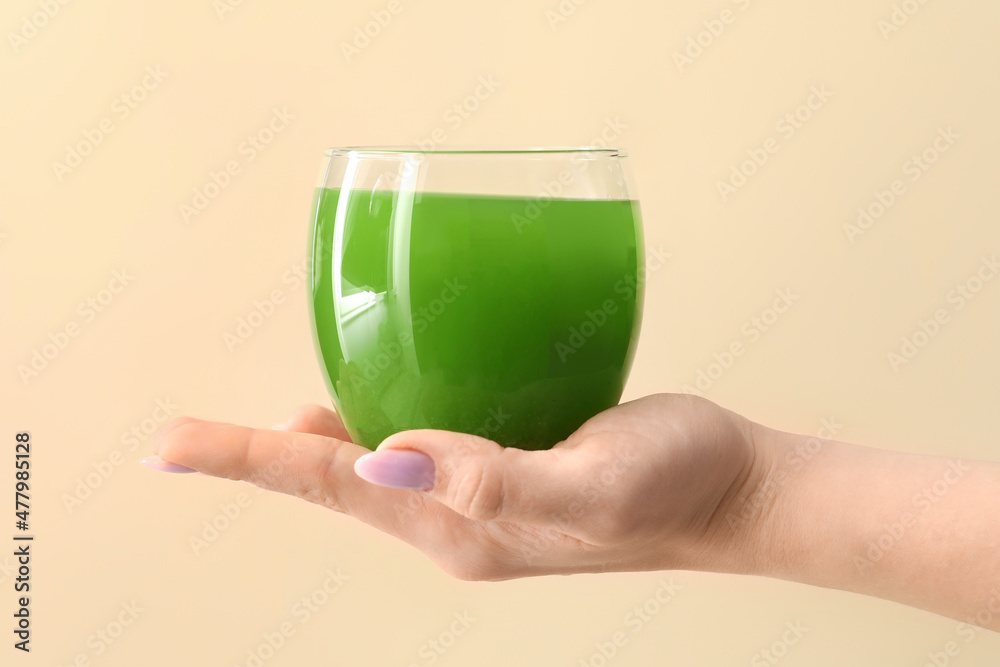 女人拿着一杯米色背景的绿色果汁
