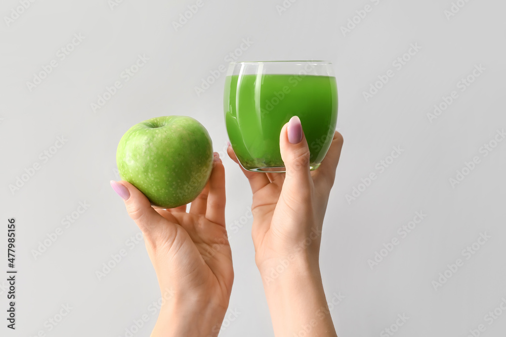 浅背景下拿着一杯绿色果汁和苹果的女人