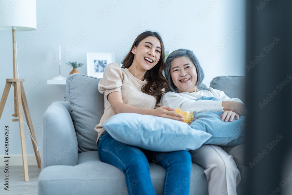 亚洲资深成熟女性和女儿坐在沙发上看搞笑电影。