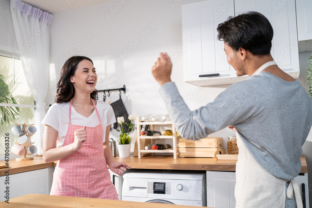 Asian attractive loving couple enjoy dance together in kitchen at home