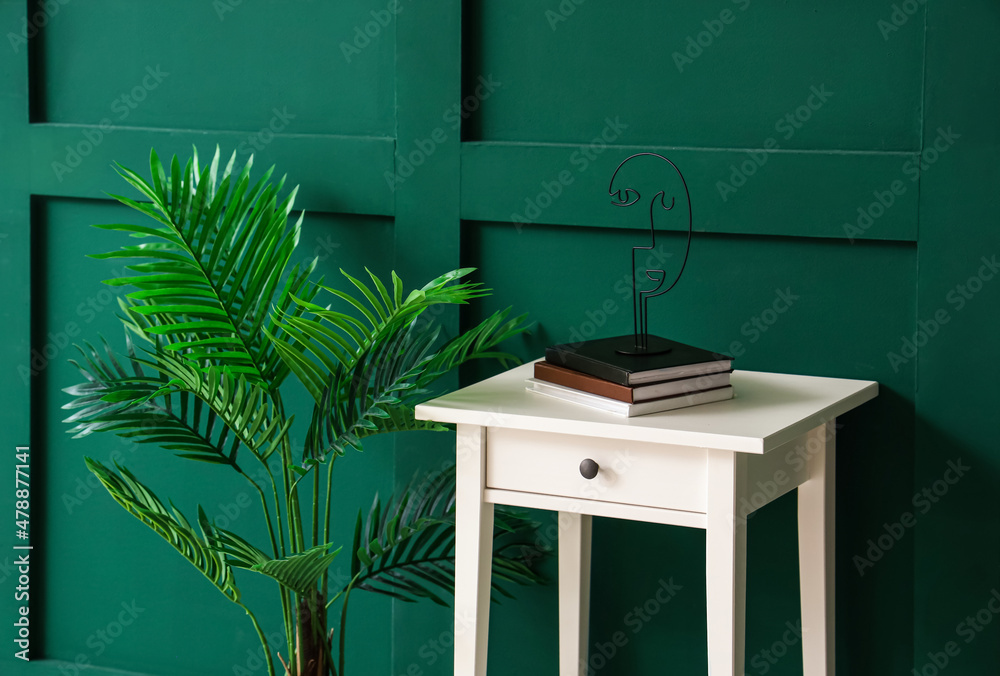绿色墙壁附近的现代餐桌，配有书籍和室内植物