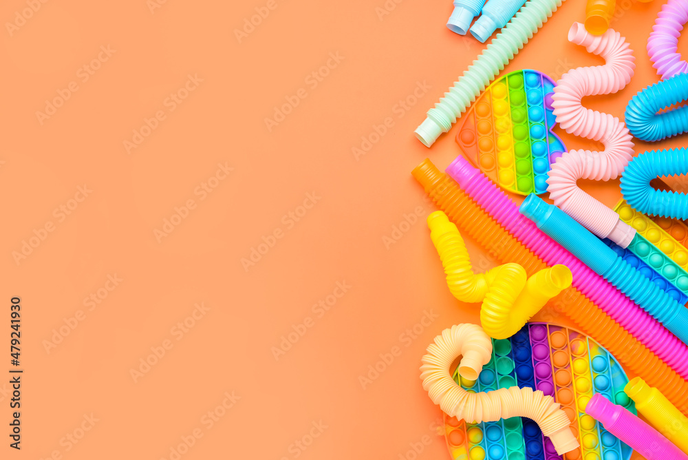 橙色背景下的彩色Pop Tubes和Pop-it坐立不安的玩具
