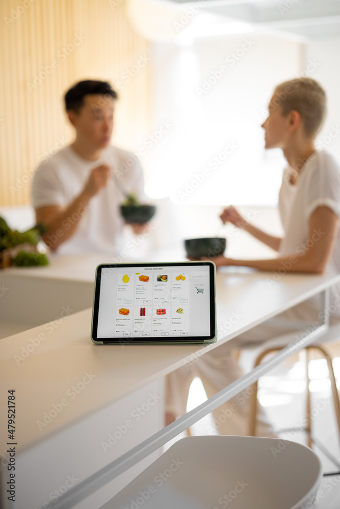 数字平板电脑，运行电子商务网站，有杂货市场和幸福的夫妇在后台吃饭