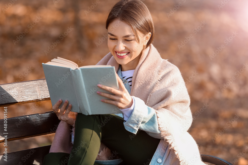 公园木长椅上有一个快乐的女人，穿着格子看书