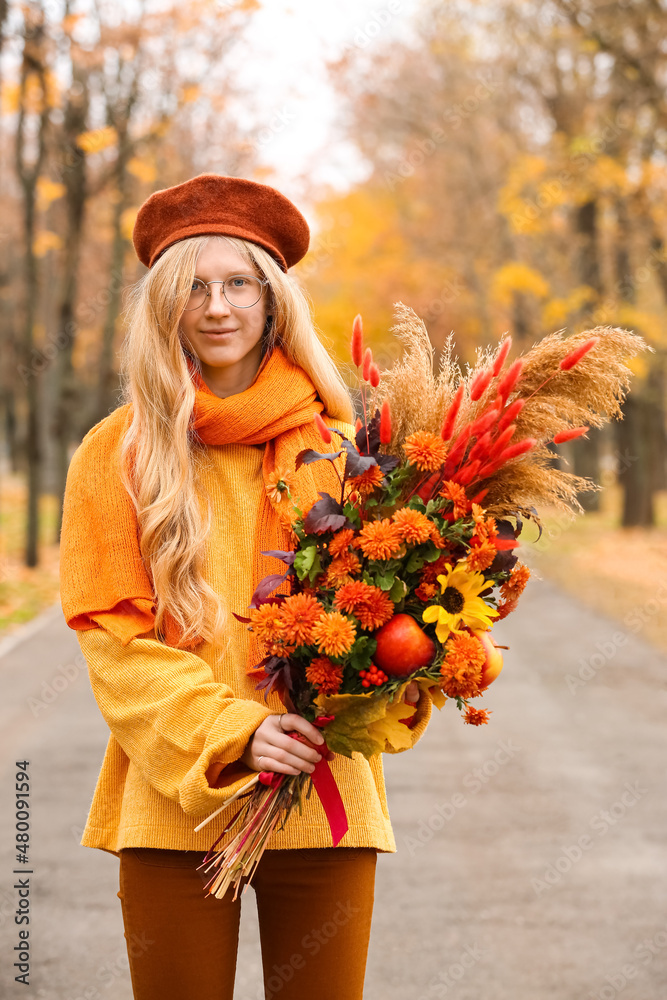 美丽的年轻女子在公园里拿着秋天的花束