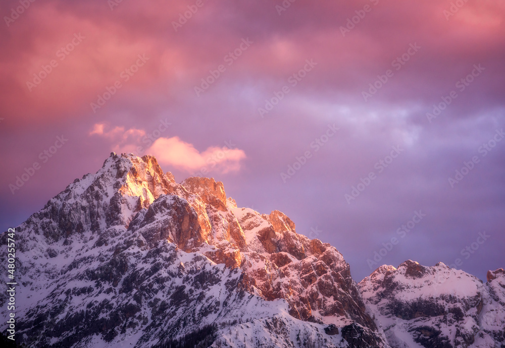 美丽的山峰在雪中，紫罗兰色的天空在冬天日落时有粉红色的云。五颜六色的土地