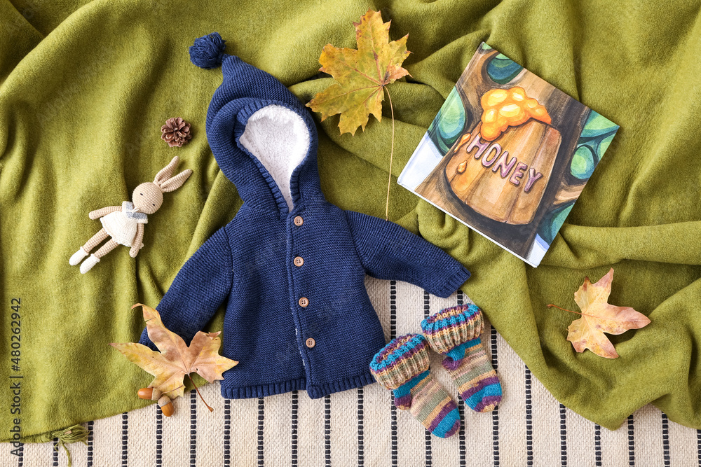 Baby clothes, toy rabbit, book and autumn decor on color fabric background