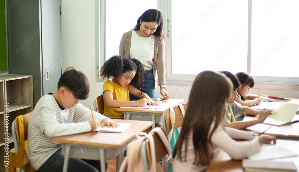亚洲女教师在小学课堂上帮助女学生写笔记