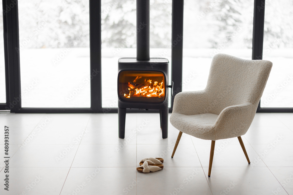 燃烧的壁炉旁舒适的生活空间，以雪地为背景，配有椅子、杯子和拖鞋