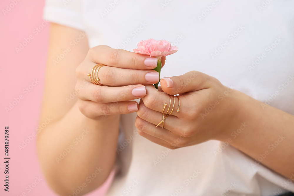 拥有美丽指甲和时尚珠宝的女士，在彩色背景上拿着美丽的康乃馨花