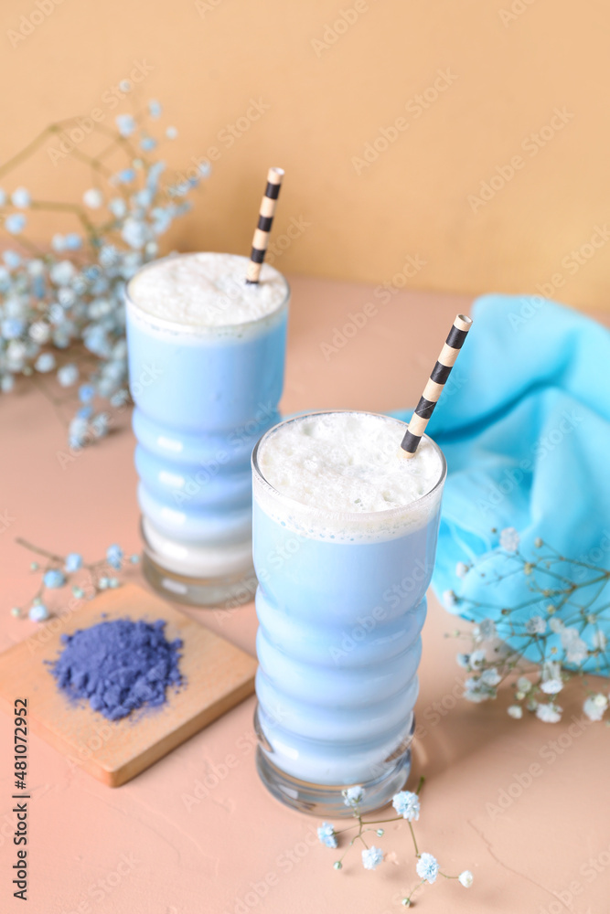 Glasses of blue matcha latte and flowers on color background