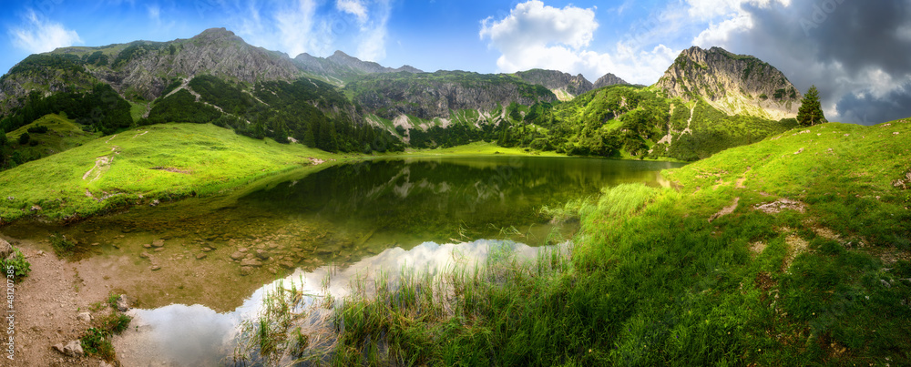 山湖全景，绿色的草地，蓝色的天空，戏剧性的云和清澈的瓦上的倒影