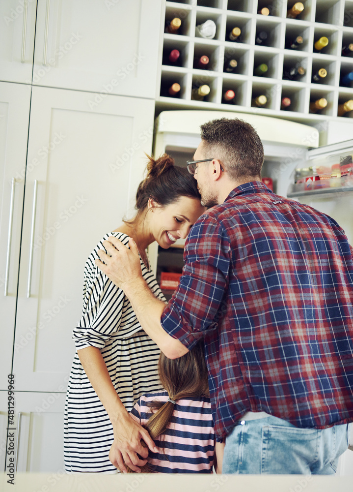 被爱捆绑在一起。一张丈夫和家人在厨房里深情亲吻妻子的照片。