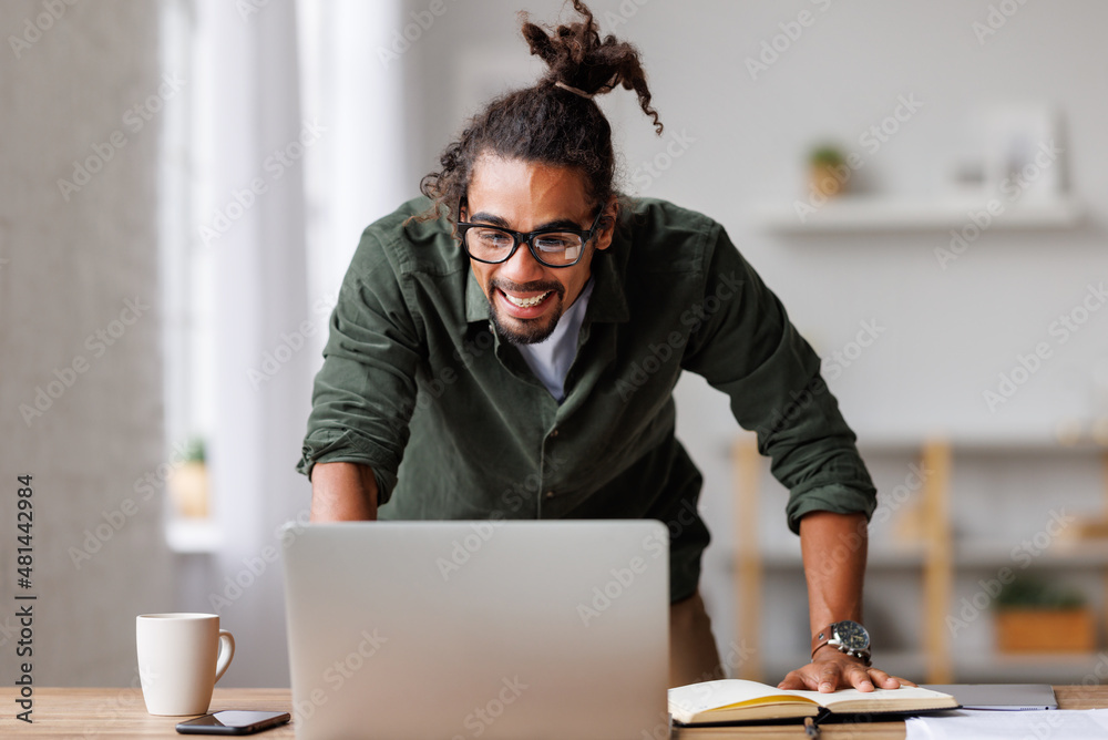 收到工作邀请后，一名欣喜若狂的非裔美国男子看着笔记本电脑屏幕感到兴奋