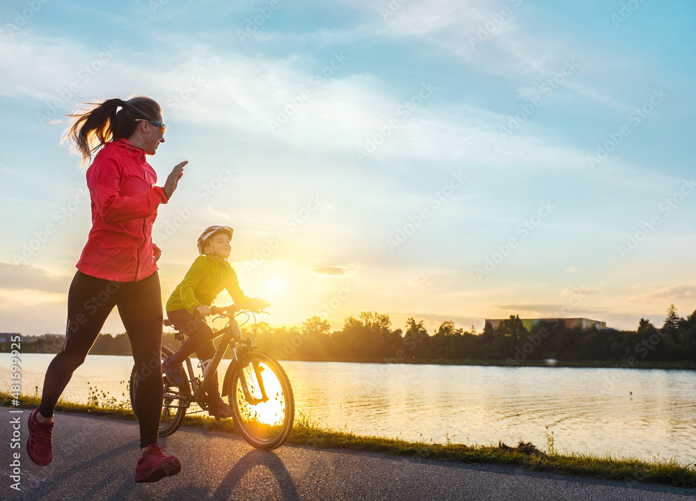 快乐的母子去户外运动。男孩戴着头盔骑自行车，妈妈在阳光明媚的日子跑步。思猴