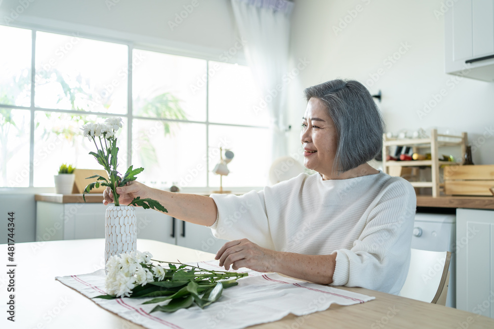 亚洲老年妇女在厨房里幸福地把鲜花放在花瓶上。